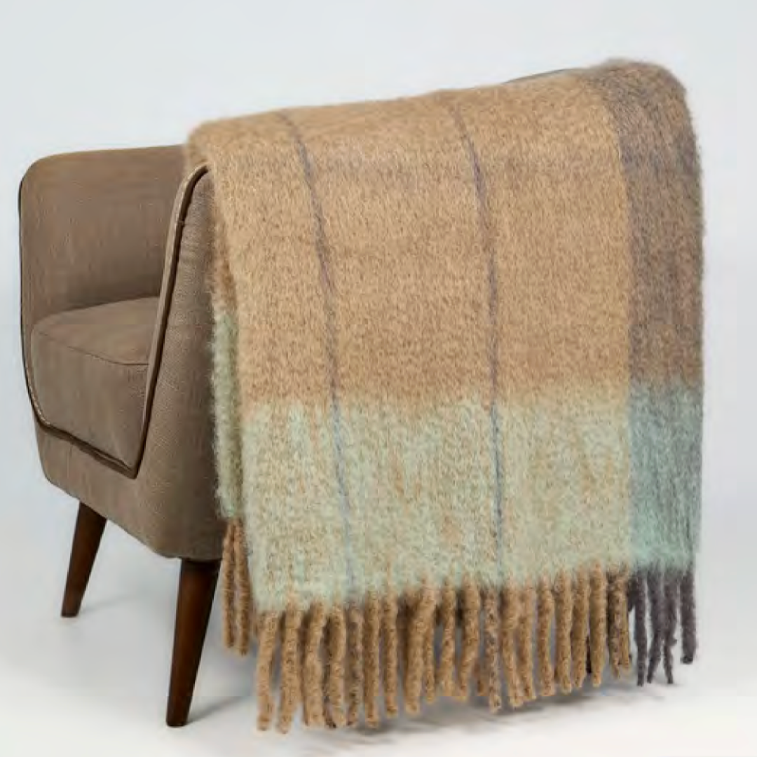 The Mantas Ezcaray Twist Frame Throw, in beige and light blue mohair, is draped over a light brown upholstered chair with wooden legs, set against a plain white background.
