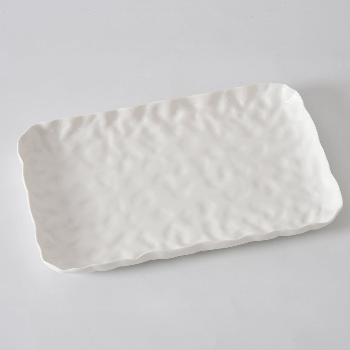 The Willow White Platter Rectangle by PAMPA BAY is a white porcelain tray with a wavy, textured surface and slightly irregular edges, shown on a light gray background.