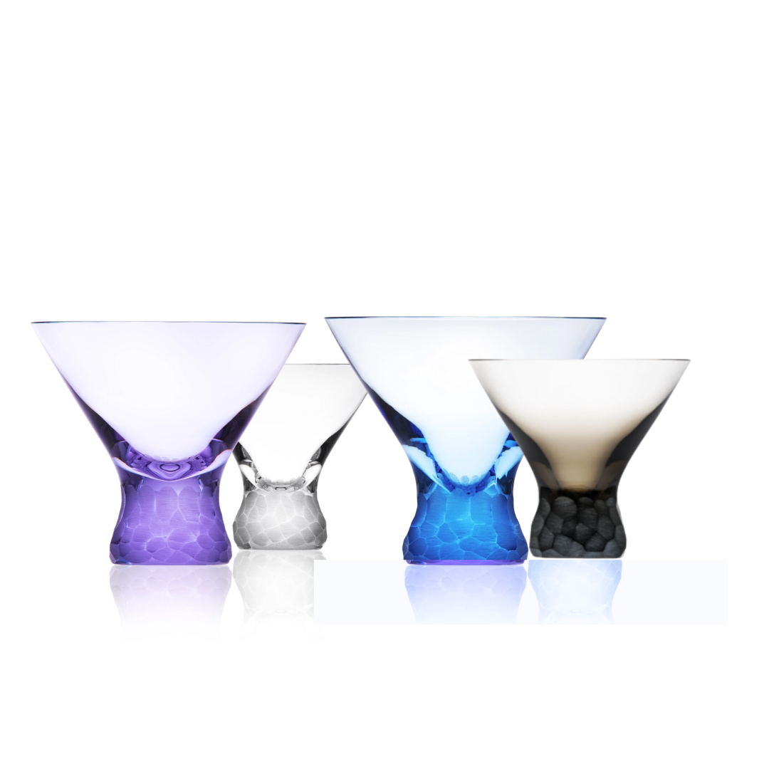 Four Pebbles Cocktail Glasses (250ml) by Moser in purple, white, blue, and grey stand on a reflective surface, highlighting the exquisite handcrafted design of this premium drinkware collection against a white backdrop.