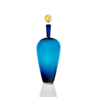 The Cariati Carmella Decanters Steel Blue & Gold features an elegant tall blue glass body, a narrow neck, and a 24K gold textured spherical stopper, displayed against a white background.