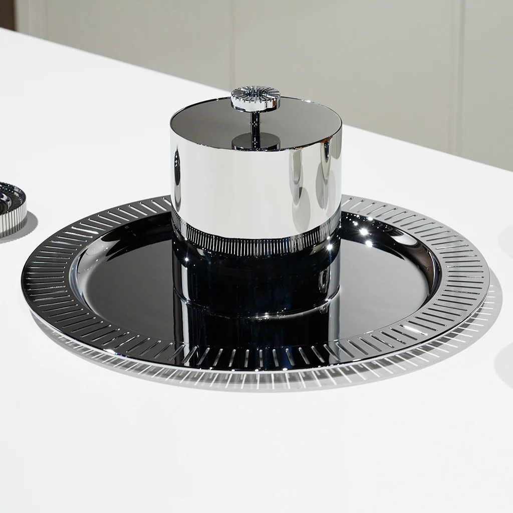 The Anna New York Striations Silver Ice Bucket with Tongs features a shiny, modern silver and black double-walled stainless steel design with a round base and cylindrical center, reflecting light on a white surface.