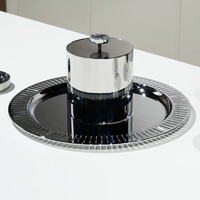 The Anna New York Striations Silver Ice Bucket with Tongs features a shiny, modern silver and black double-walled stainless steel design with a round base and cylindrical center, reflecting light on a white surface.