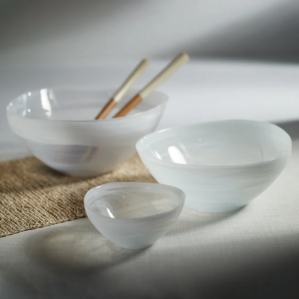 Three Monte Carlo White Alabaster Bowls by Zodax in different sizes are arranged on a light surface, with two wooden chopsticks placed in the largest bowl and part of a woven mat visible underneath.