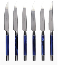Six Conty Steak Knives by Capdeco, each with shiny silver serrated blades and glossy blue handles with silver accents, are lined up vertically—a stylish French-made set of six shown against a white background.