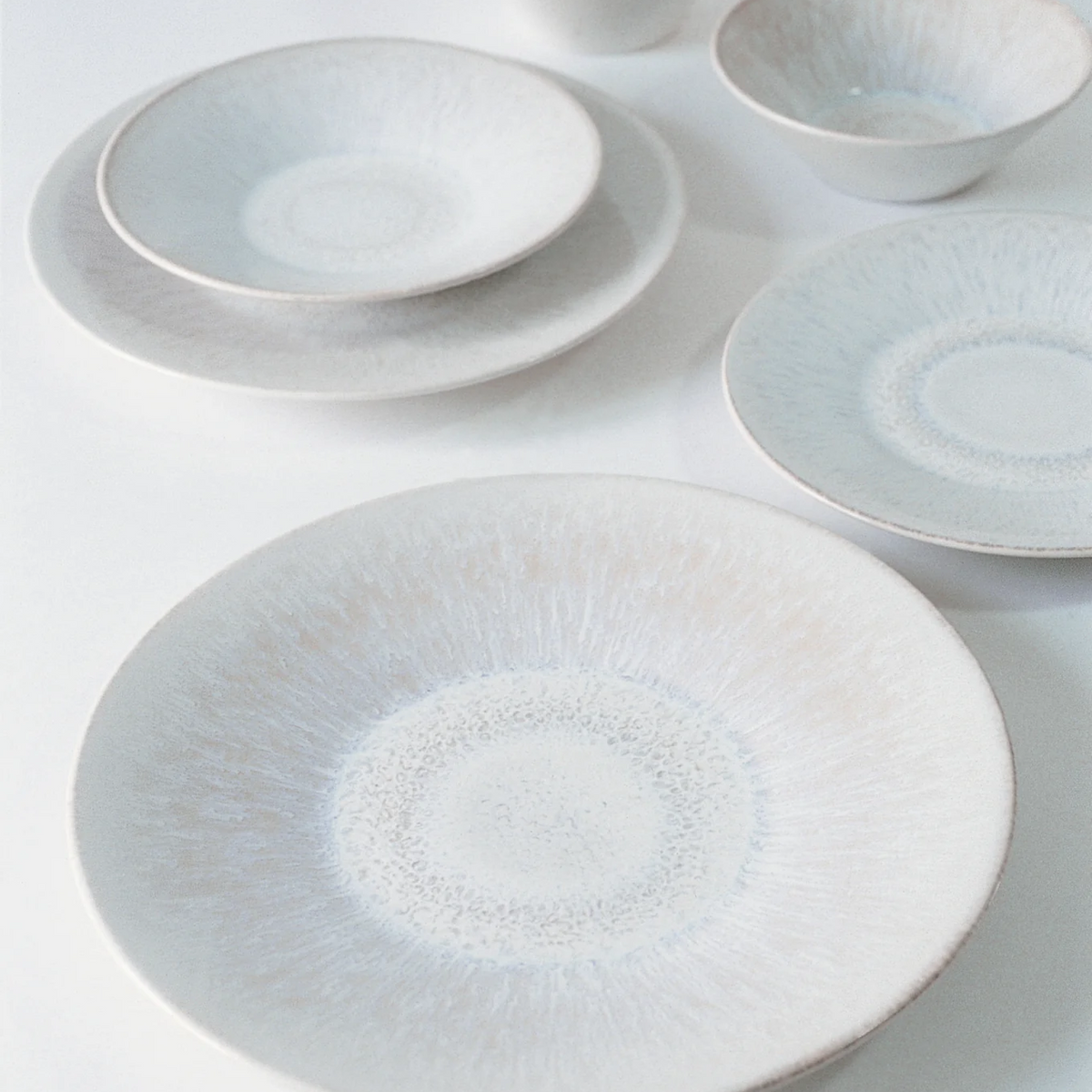 The Vuelta White Pearl set by Jars - Rosenthal features white ceramic plates and bowls with blue and beige radial patterns, a minimalist atoll glaze, and includes a dinner plate. Elegant and dishwasher safe, they look stunning on any table.