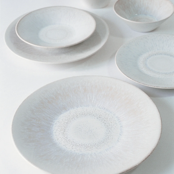 The Vuelta White Pearl set by Jars - Rosenthal features white ceramic plates and bowls with blue and beige radial patterns, a minimalist atoll glaze, and includes a dinner plate. Elegant and dishwasher safe, they look stunning on any table.