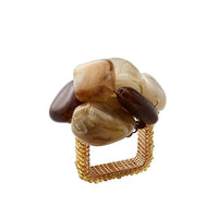 The Kim Seybert Sea Stone Napkin Ring Beige Set of 4 features square gold mesh rings topped with large, smooth stones in brown, beige, and cream clustered on top.