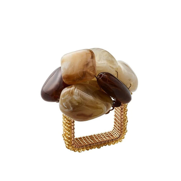 The Kim Seybert Sea Stone Napkin Ring Beige Set of 4 features square gold mesh rings topped with large, smooth stones in brown, beige, and cream clustered on top.