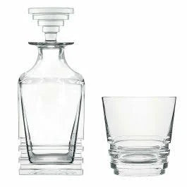 The Saint-Louis Oxymore Drinkware set features a clear glass decanter with a geometric, stepped stopper beside a matching tumbler, both with angular stacked bases, exemplifying contemporary French glassware style.