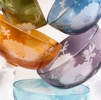 A close-up of six vibrant Polspotten Peony Coupe Glasses stacked together, each with a sandblasted floral pattern. The Multicolor Set includes blue, purple, amber, green, turquoise, and one additional hue.
