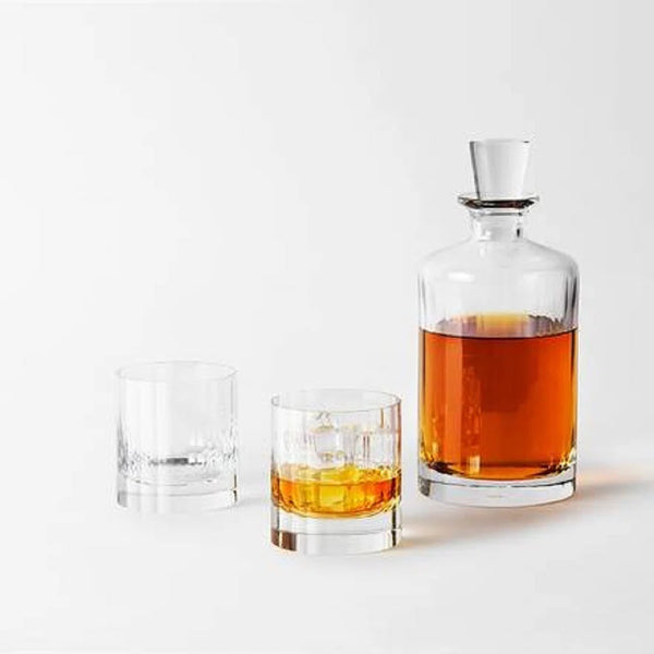 The Richard Brendon Fluted Shot Glass Set of 2 stands beside a mouth-blown glass decanter filled with amber liquor—an elegant barware addition—displayed on a white surface against a plain white background.