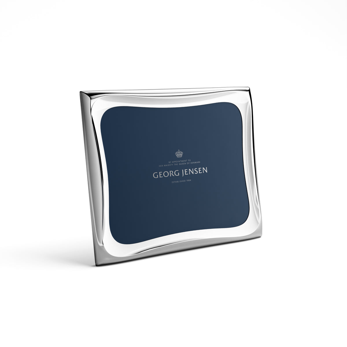 The Georg Jensen Cobra Stainless Picture Frame, featuring smooth, curved edges and a silver finish, stands on a white background. Its dark blue center insert displays the brand name, crown logo, and smaller text.