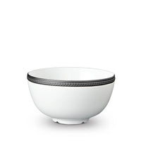 The Soie Tressée Black Dinnerware by L'Objet is a white ceramic bowl with a slightly flared rim, accented by a textured dark gray band around the top and resting on a small, round base.