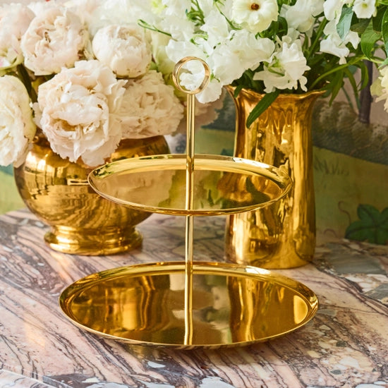 The Sinta 2 Tier Stand by Aerin rests on a marble surface, with gold vases of white and blush flowers in the background, creating an elegant and luxurious setting.