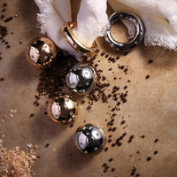 Platinum-plated spherical and ring-shaped objects from the Stars Spice Jewels Salt & Pepper Set by L'Objet are displayed on a textured surface with black peppercorns, coarse salt, and white fabric.