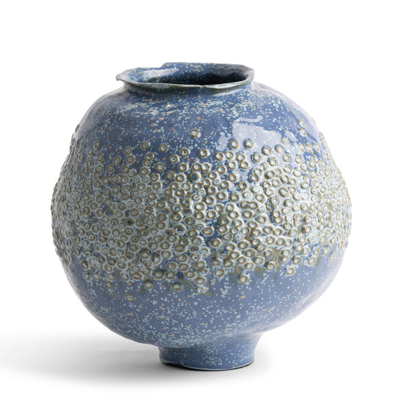 The Ashley Vase - Blue by FlowDecor Inc. is a round ceramic vase with a narrow opening and a textured surface that showcases raised circular patterns accented with white speckles. This eye-catching decorative piece is photographed against a plain white background.