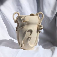 The Floral Vase by Terroso Studios is a beige, handmade ceramic piece featuring abstract, flowing handles and sculpted shapes in a twisting organic design, beautifully set against draped white fabric.