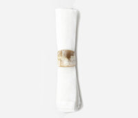 A white cloth napkin is neatly rolled and secured with a wide, glossy, light brown James Natural Horn Napkin Ring from Blue Pheasant on a plain white background.