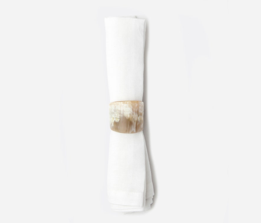 A white cloth napkin is rolled up and secured with the James Natural Horn Napkin Ring set from Blue Pheasant, featuring a beige, marble-patterned finish, set against a plain white background.