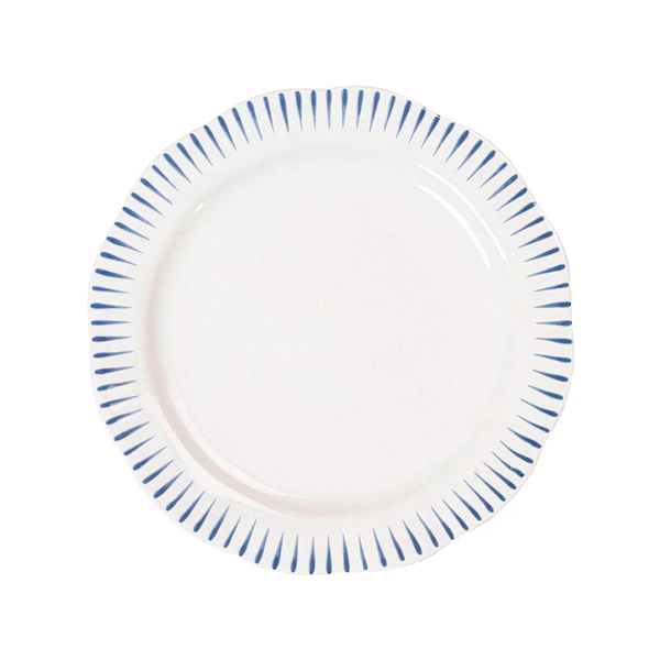 The Sitio Stripe Dinnerware by Juliska is a round white dinner plate with a scalloped edge, whitewash glaze, and evenly spaced short Delft blue lines along the rim.