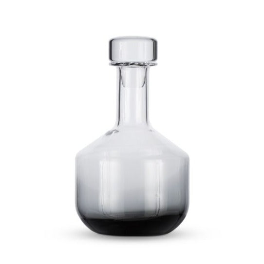 A Tom Dixon Tank Black Whiskey Decanter with a round stopper, wide base, and narrow neck is photographed against a plain white background.