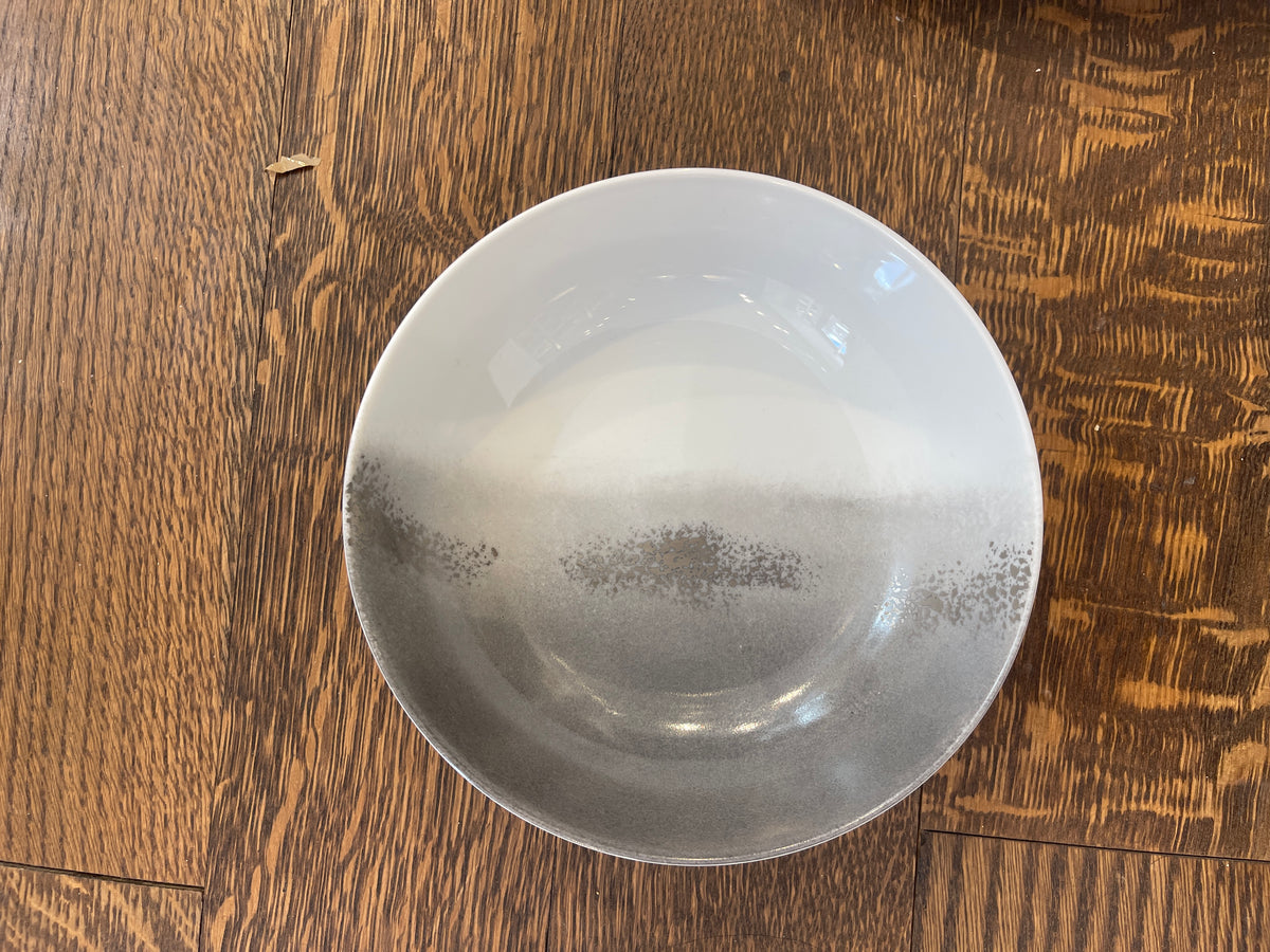The Marie Daâge Maarie Daâge Horizon Platinum Dinnerware, a hand-painted white ceramic bowl with a gray gradient, made in France, rests on a natural wood grain surface.