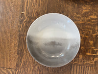 The Marie Daâge Maarie Daâge Horizon Platinum Dinnerware, a hand-painted white ceramic bowl with a gray gradient, made in France, rests on a natural wood grain surface.