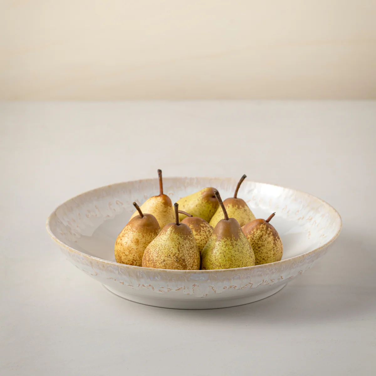 A Casafina Taormina Dinnerware White bowl, made in Portugal, holds eight speckled pears on a light surface with a simple pale background.