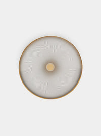 A circular piece from the Oskar Dinnerware collection by Raynaud, adorned with fine, concentric rings radiating from a central hub and reminiscent of Limoges porcelain craftsmanship, is displayed against a plain white background.