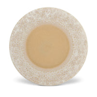 The Terra Platter Charger Dusty Rose by L'Objet features a smooth tan center and a textured, speckled beige and white rim, displayed on porcelain placemats from an overhead view against a white background.