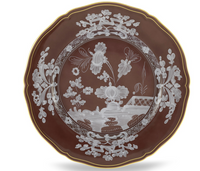 The Oriente Italiano Castagna plate by Ginori 1735 features a brown base with detailed white floral and basket designs at the center and border, accented by a thin gold rim—an elegant addition to the tableware set.