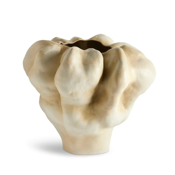 The Timna Latte Vase Short by L'Objet is a beige porcelain vessel with an irregular, sculptural shape and matte texture inspired by the windswept forms of the Arava desert near King Solomon's Mines.