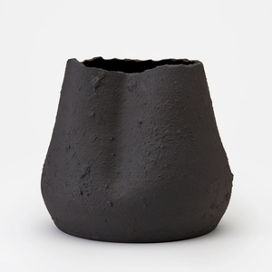 The Phoebe Vase by Dumae features a black matte finish, uneven textured surface, and an irregular wavy rim, highlighting its sculptural design against a plain white background.
