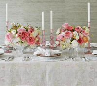 A beautifully set table features pink and white floral centerpieces, tall candles in pink holders, elegant glassware, silverware, and the Kim Seybert Giverny Tablecloth in Mint & Multi for an artistic touch.