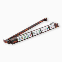 The Oh My Mahjong Mahjong Rack & Pusher Set - Tortoise Shell holds your tiles in style, featuring a row of tiles with colorful symbols and one upright at the end—a chic game night accessory for any set.