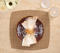 A square, brown and white Twill Placemat Set of 4 - Brown & White topped with a dark plate, a cream-colored napkin, and a metallic floral napkin ring.