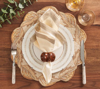 Elegant table setting featuring a white plate, beige napkin with the Kim Seybert Twist Napkin Ring Set of 4 in Brown & Gold, silver fork and knife, clear wine glasses, leafy placemat, and green eucalyptus on a wooden table.