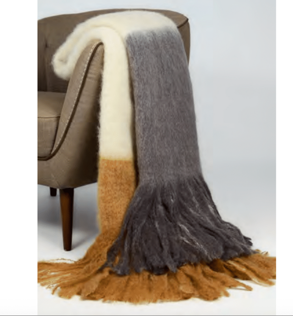 The Mantas Ezcaray Color Block Throw in Grey/Tan, featuring long fringed ends, is draped over a light brown chair and adds a cozy, modern touch to any space.