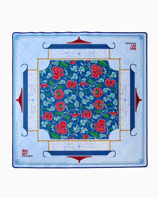 Oh My Mahjong’s Mahjong Mats feature a square neoprene design with a central blue floral pattern of red and pink flowers, a blue and gold border, and sections with light blue text and Mahjong motifs on white.