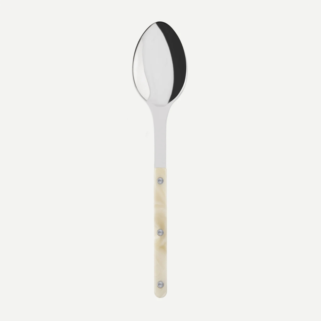 The Sabre Bistro Horn Serving Spoon, made in France, features a shiny oval stainless steel bowl and a light marbled handle with three metal rivets, displayed against a plain white background.