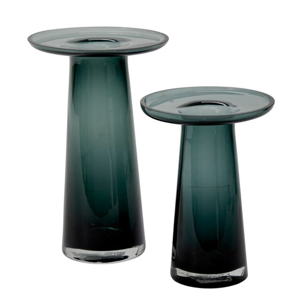 The Accent Decor Topple Vase Green features two modern glass vases in dark green with clear bases and wide, flat tops, displayed side by side at varying heights—ideal as stylish coffee table decor.