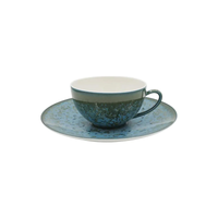 The Nymphea Dinnerware cup and saucer by Jaune De Chrome feature a speckled blue-green glaze with a rustic, handmade look and a light off-white cup interior. Made in France.