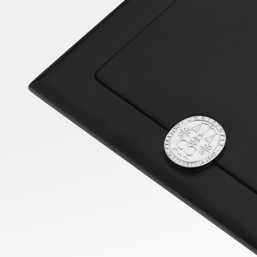 A Christofle Fidelio Silver Plated Frame 7x9.5 in sleek black features a silver coin on its corner, set against a plain white background.