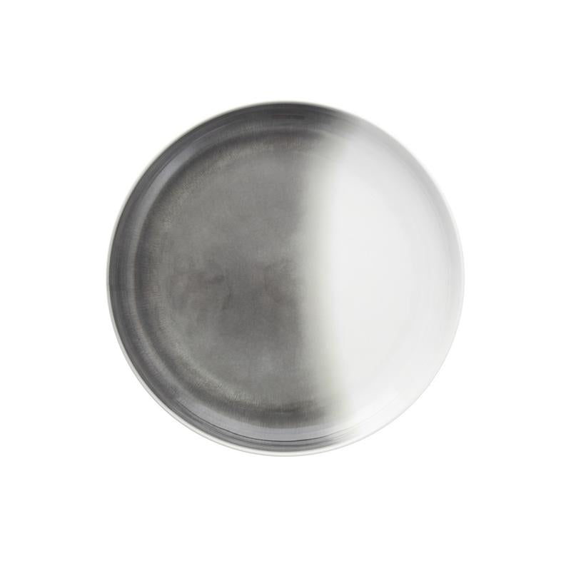 The Fortessa La Cotera Melamine Dinnerware Gray plate features a round, metallic look with a matte gradient—half dark, half light. Stylish and dishwasher safe, this durable piece is perfect for modern dining and is set against a plain white background.