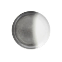 The Fortessa La Cotera Melamine Dinnerware Gray plate features a round, metallic look with a matte gradient—half dark, half light. Stylish and dishwasher safe, this durable piece is perfect for modern dining and is set against a plain white background.