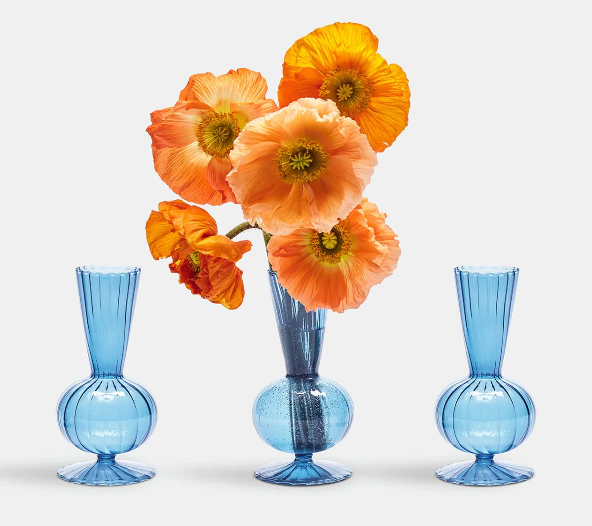 The Kim Seybert Tess Bud Vase Set of 3 in blue is displayed on a plain white background. The center vase holds orange and yellow poppy flowers, while the two side vases are empty.