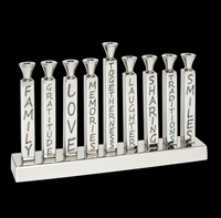 Illuminate your Hanukkah with the Mimi Menorah from Inspired Generations. This eye-catching silver aluminum candle holder features candles labeled Family, Gratitude, Love, Memories, Togetherness, Laughter, Sharing, Traditions, and Smiles. Set against a dramatic black background, the Mimi Menorah makes a meaningful gift and elegant centerpiece for your holiday celebrations.