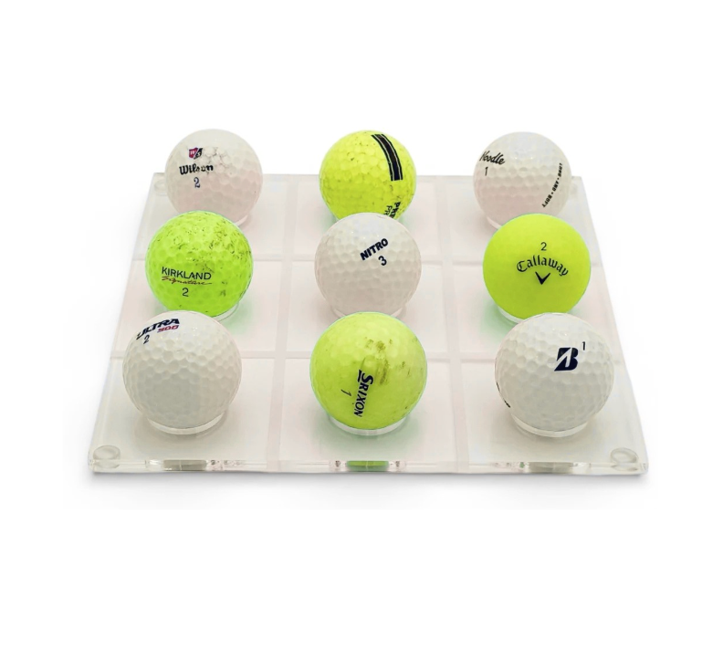 The Luxe Dominoes Golf Ball Tic Tac Toe set features nine white and yellow golf balls from different brands, arranged in a 3x3 lucite grid—each with visible logos and numbers, making it a perfect gift for golf lovers.
