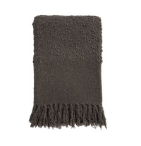 The Murphy Throw - Midnight by Pom Pom At Home is neatly folded, showcasing its fluffy bouclé texture and thick fringe tassels along one edge, set against a plain white background.