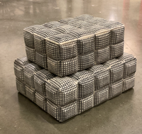 Two stacked Cubie Box poufs by A Sanoma Inc with a black grid pattern on cream sit on a concrete floor, adding an edgy decorative accent to your home.